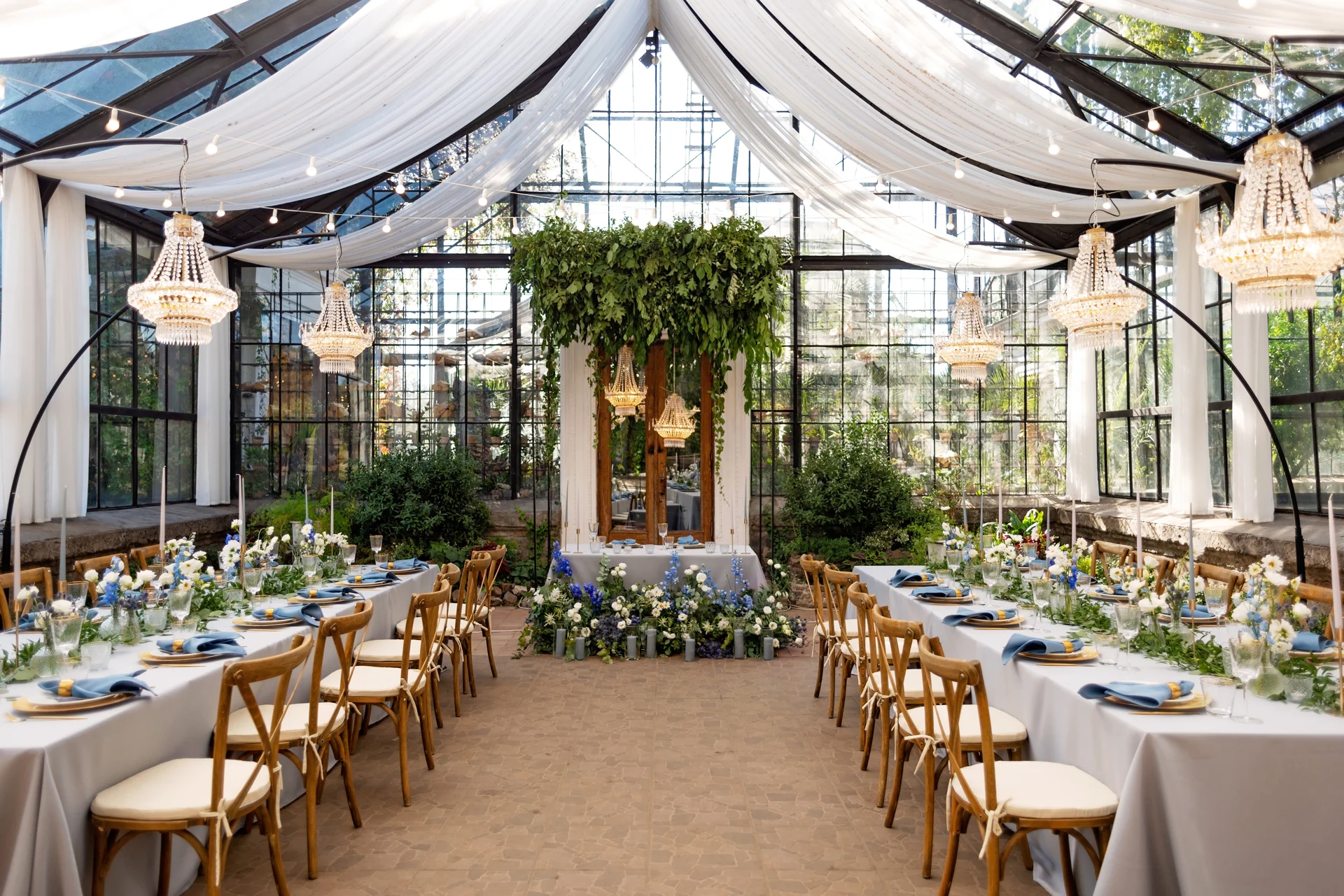 Glass garden pavilion filled with greenery, chandeliers and beautifully set reception tables